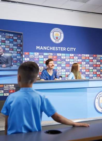 People sat in the press confeerence room on the Manchester City Stadium Tour