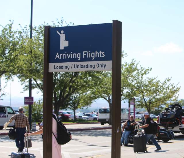 The external arrival zone at Rapid City Regional Airport as passengers with luggage wait for transportation.