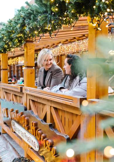 2 people stood on balcony of Christmas Markets with out of focus christmas tree in the foreground