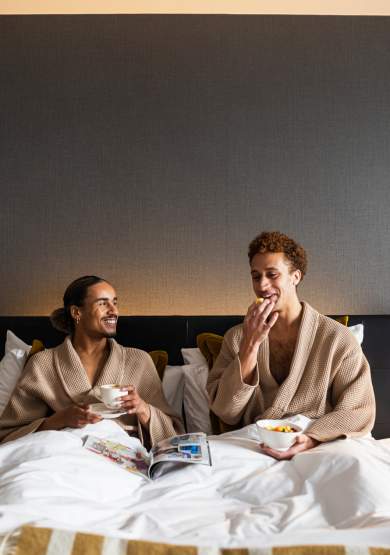 Couple in hotel bed in dressing gowns eating breakfast and drinking coffee