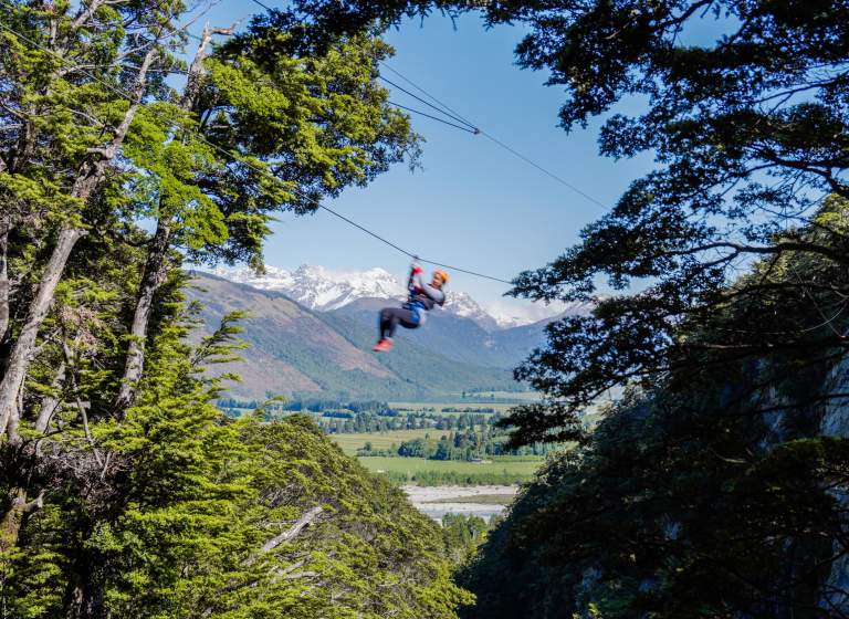 Person ziplining with snow-covered mountain in the back