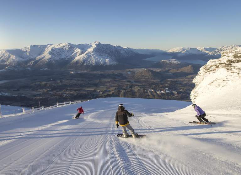 Snowboarders and skiers riding down snowy mountain