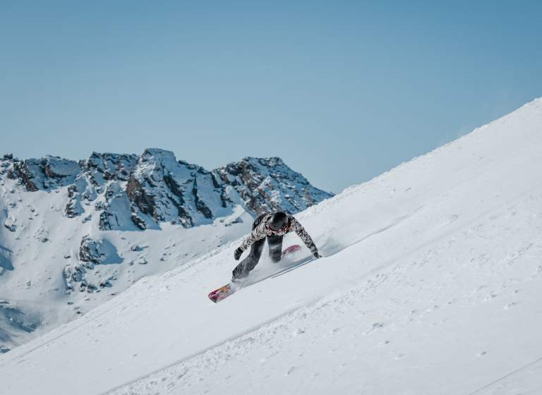 Spring snowboarder shredding a slope at The Remarkables with blue sky and mountains in the background