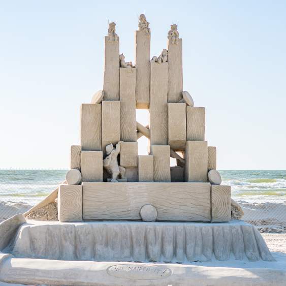 Sand sculpture depicting small men playing instruments and building a structure out of blocks.