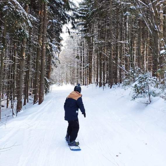 Man snowboarding down wooded trail