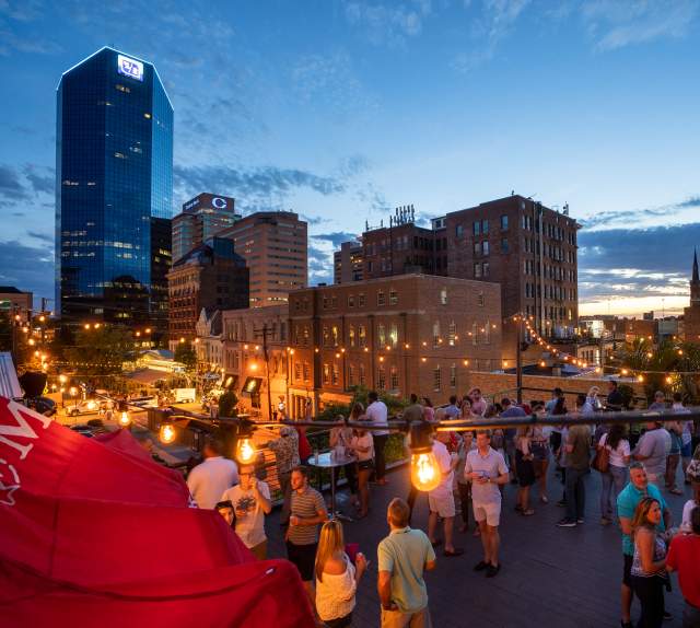 Roof top bar, Belle, filled with patrons enjoying drinks as the sun goes down behind the city skyline.