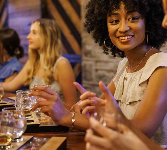 Women at a bar tasting bourbon and talking.