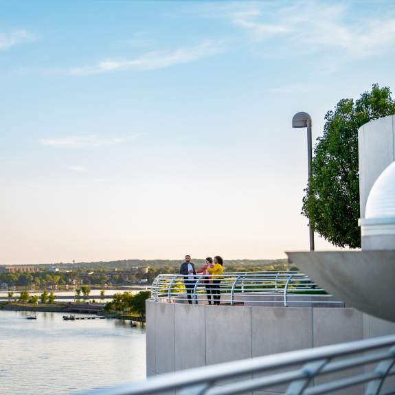 A wide view of three people enjoying drinks on the rooftop of Monona Terrace with Lake Monona and the sunset in the background