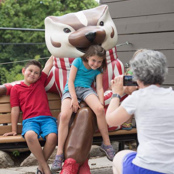 A woman takes photos of two young kids sitting on a Bucky Badger statue at Henry Vilas Zoo