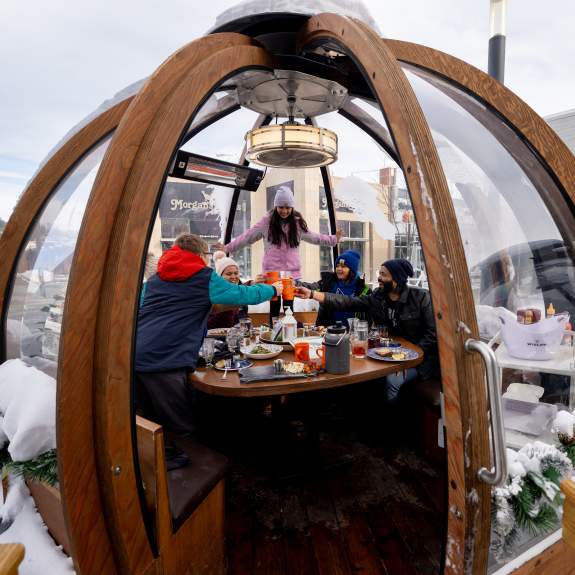 Friends enjoying drinks and dining in an outdoor winter dome at Cafe Hollander in Madison, with snow surrounding the dome.