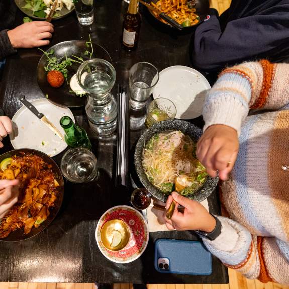 Aerial view of a dining table with various dishes, drinks, and people enjoying a meal together, creating a vibrant culinary experience.