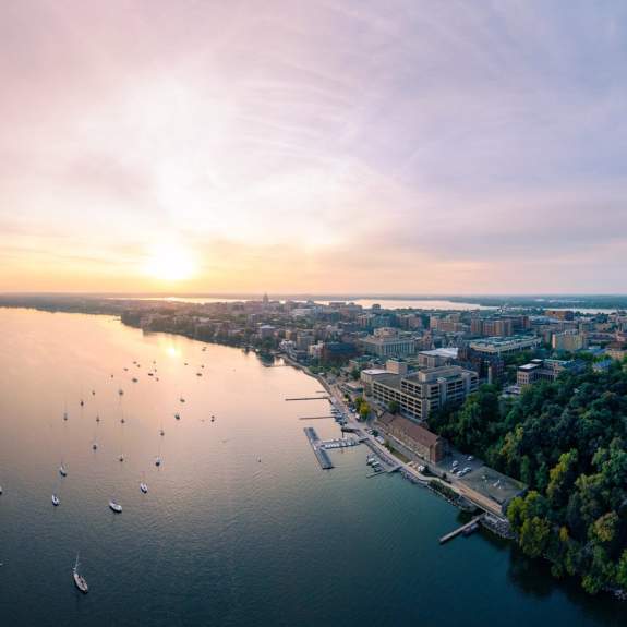 A wide drone image of the city at sunset with Lake Mendota in the foreground