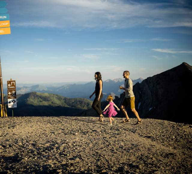 A happy family hiking on top of a mountain with ski trail sign markings