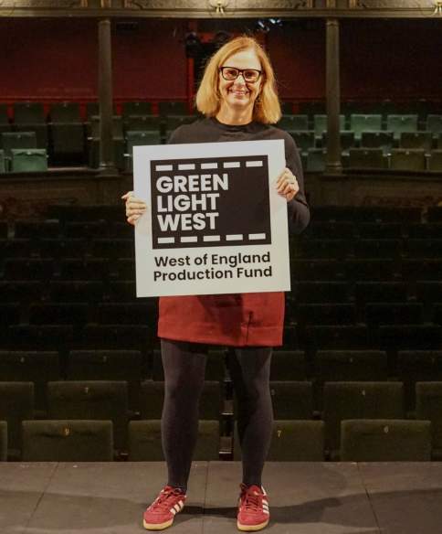 Mayor Helen Godwin on stage at Bristol Old Vic holding a sign that says Green Light West