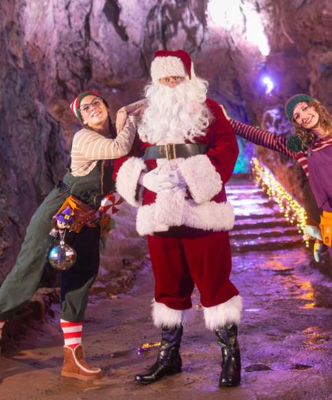 An elf wearing a green jumpsuit, Santa wearing a red suit and an elf wearing a purple jumpsuit