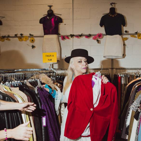 A person holding up a velvet red suit jacket at a vintage store.
