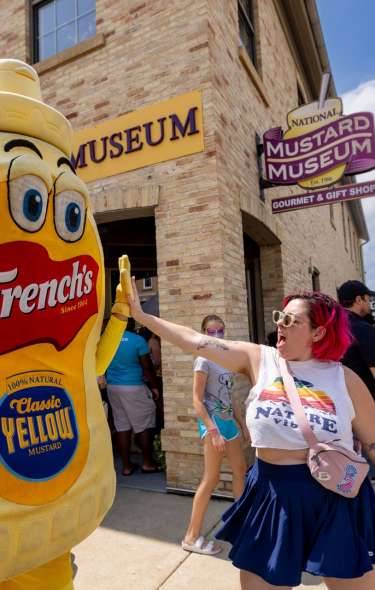 A white woman high fives a person wearing a mustard costume outside the National Mustard Museum in Middleton
