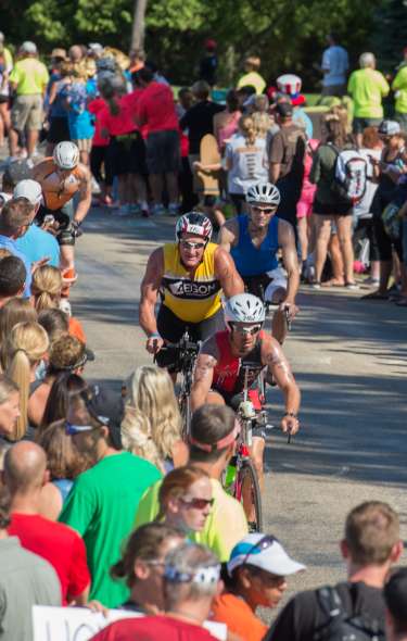 Dozens of people line the streets to watch bicyclists race in the IRONMAN race