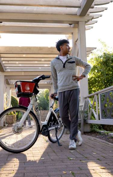 A young Black man stands next to his electric bike while taking in the views at the Allen Centennial Gardens