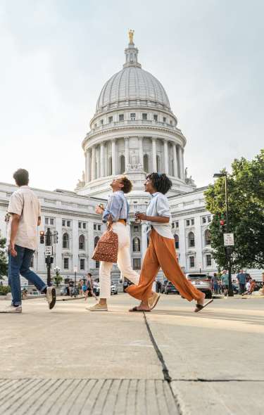 A group of four young adults walk in front of the Capitol building during a summer evening.