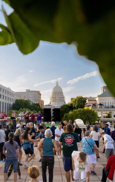 Dozens of people dance to live music on the rooftop of Monona Terrace. The Capitol building is far off on the horizon.