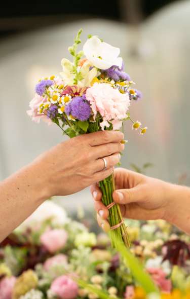 One person hands another person a small bouquet of purple and white flowers