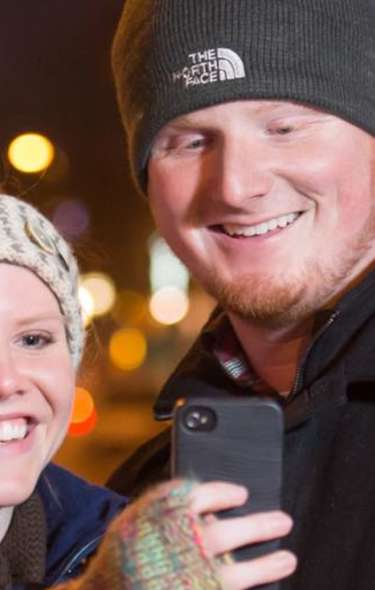 A white man and a white woman take a selfie on State Street at night with the Capitol building in the distant background