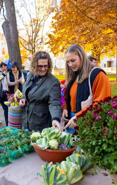 Two white women look over a table of vegetables at the Dane COunty Farmers Market in Fall