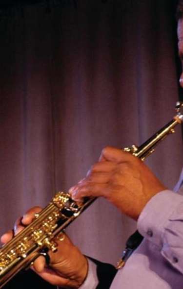 A Black man plays an alto saxophone on stage in front of a piano