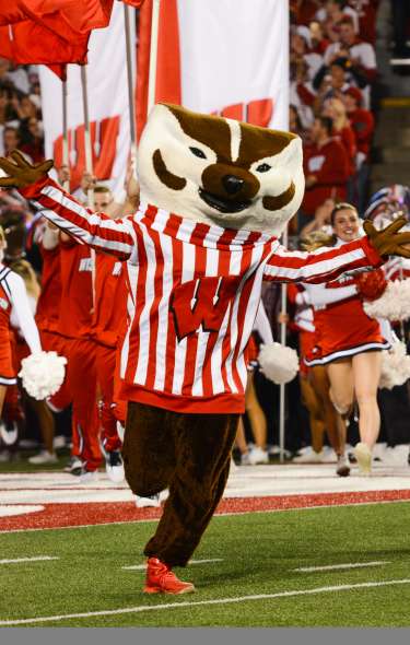 Bucky Badger runs out onto the field at Camp Randall stadium followed by UW Badger cheerleaders and band members.