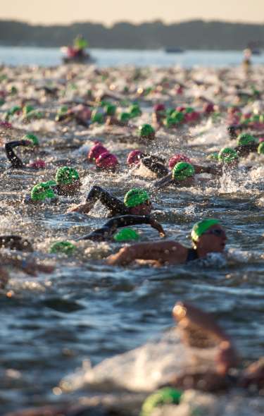 Dozens of people in green swim caps swim in a lake during the Ironman race
