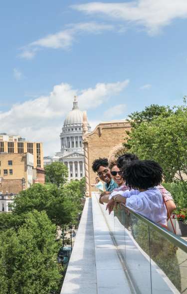 A group of four young adults peer over a rooftop patio with the Capitol and Orpheum Theater in the background