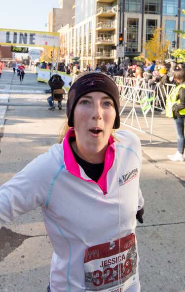 A woman wearing running gear rings a bell after crossing the finish line at a race in downtown Madison