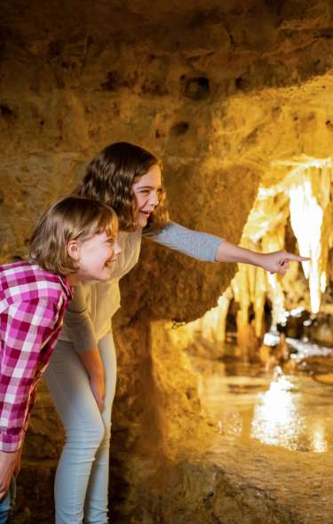 Two young girls point at formations inside of a cave at Cave in the Mounds