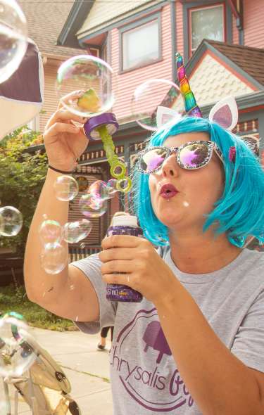 A woman in a cyber blue wig and cat ears blows bubbles during a festival on Willy Street.