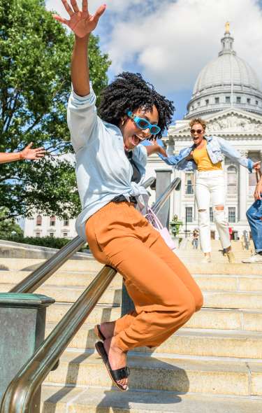 A Black woman slides down a railing with joy as three friends around her cheer in front of the Capitol building