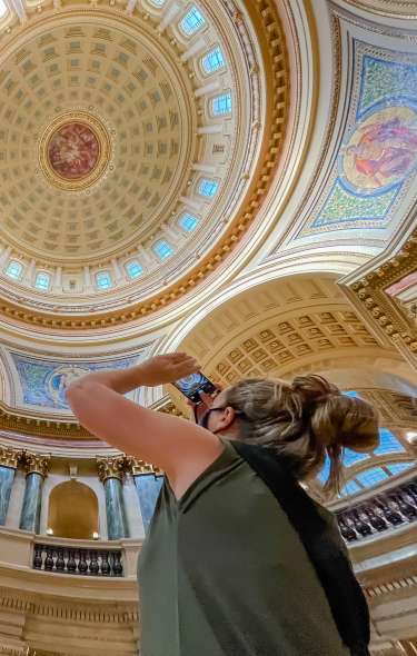 A white woman uses her phone to take a picture of the rotunda ceiling inside the Wisconsin State Capitol