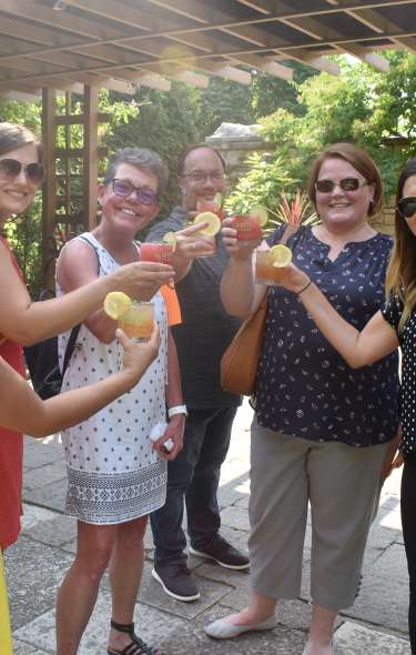 A group of young adults clink cocktail glasses while standing outside on a patio