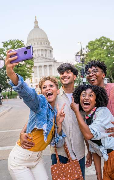 A group of a four friends taking a selfie in front of the Wisconsin State Capitol building on State Street.