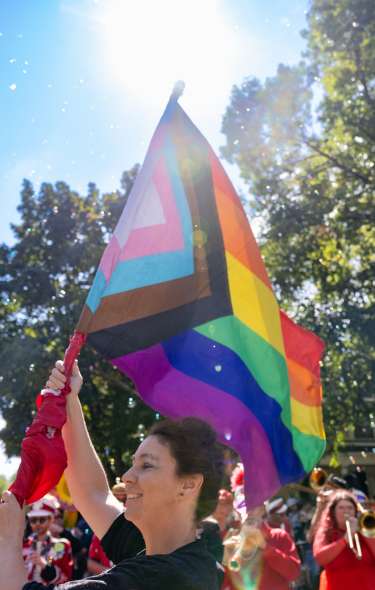 A white person holding up an LGBTQ+ pride flag while walking in a parade.