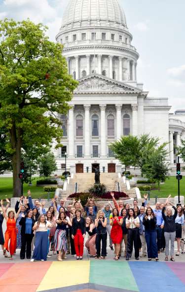 A group of people standing on the Pride crosswalk that cross State Street in front of the Wisconsin State Capitol building.