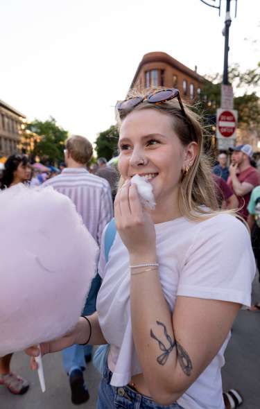 A white woman white blonde hair smiling while eating pink cotton candy at the Madison Night Market.