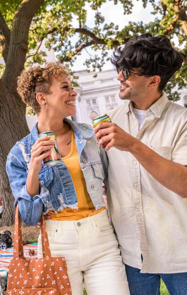 A man and woman couple hold cans and look at each other outside of the Wisconsin State Capitol during Concerts on the Square
