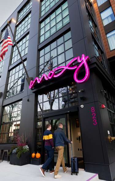 Two men with suitcases walking into the Moxy Hotel.