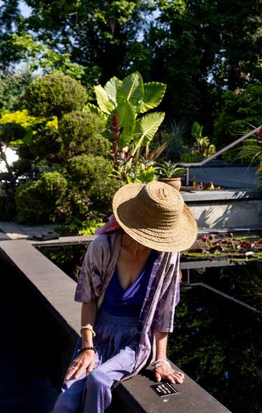 A woman looks down into a clear reflection pond with lilly pads on top in front of the Thai Pavilion at Olbrich Botanical Gardens