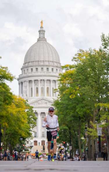A white male triathlete runs in the Ironman race with the Capitol building in the background