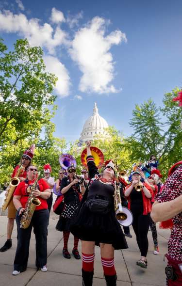 A member of the Forward marching band fists pumps in excitement surrounded by the band with the State Capitol in the background