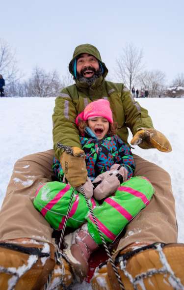 A man and a young girl slide down a snowy hill on a sled with