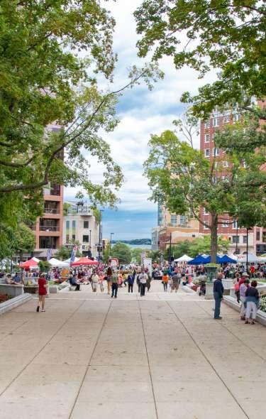 A wide view of the Farmer's Market at Capitol Square showing hundreds of people walking around and looking at booths