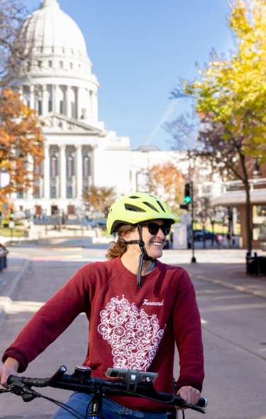Two white women smile as they ride bikes with the Wisconsin State Capitol in the background